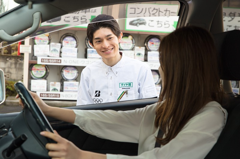 運転席の窓越しに会話をする男性スタッフと女性客｜タイヤ館